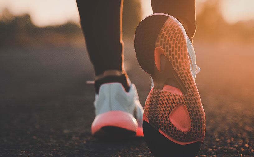 Gros plan sur les chaussures de sport d’une personne en mouvement au lever du soleil, symbolisant l’idée de parcours et de cheminement.