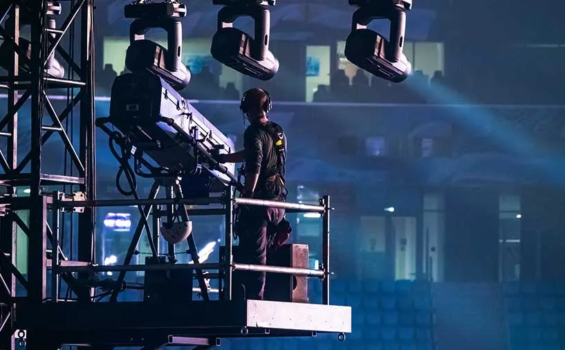 Technicien du spectacle vivant opérant un projecteur en hauteur dans une salle de concert ou de spectacle.