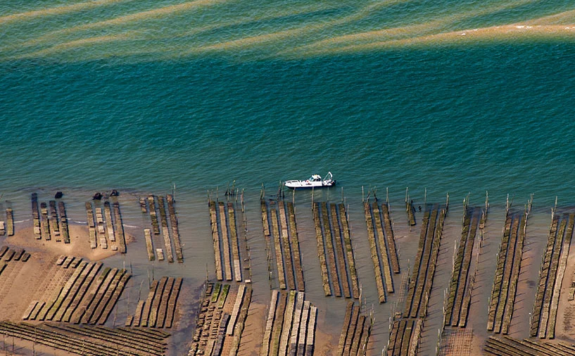 Vue aérienne d’un parc ostréicole avec une embarcation en mer, illustrant les activités conchylicoles sur le littoral néo-aquitain