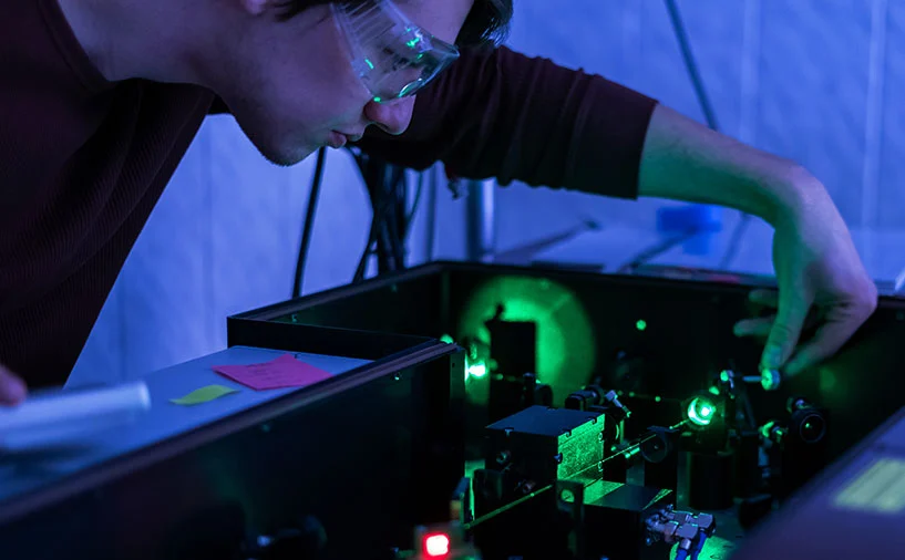 Un technicien en lunettes de protection règle un système optique laser dans un environnement de laboratoire spécialisé en photonique
