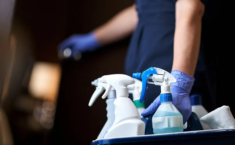 Un agent équipé de gants de protection manipule un chariot de nettoyage contenant des produits d’entretien et désinfectants