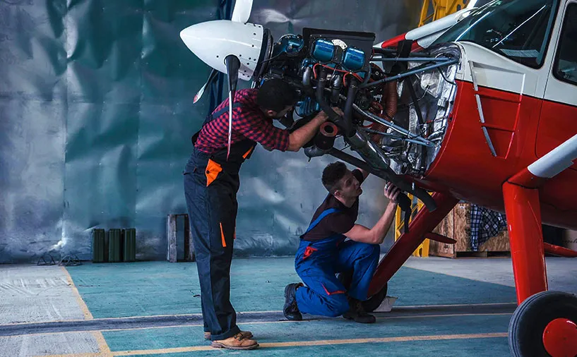 Deux techniciens effectuent une opération de maintenance sur le moteur d’un avion léger dans un hangar