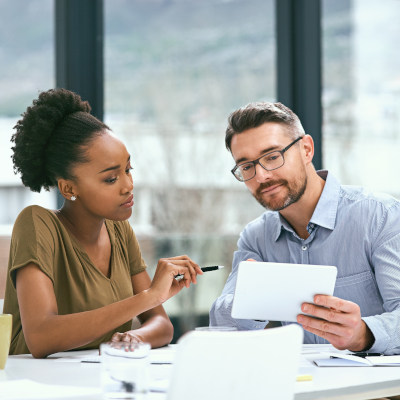 Une femme et un homme en discussion professionnelle, consultant une tablette, illustrant la prévention et l’évaluation différenciée des risques au travail.